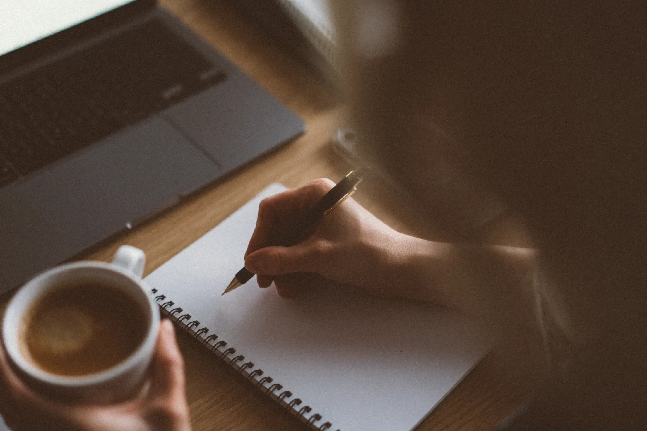 Hand writing three priorities in a notebook beside a coffee cup